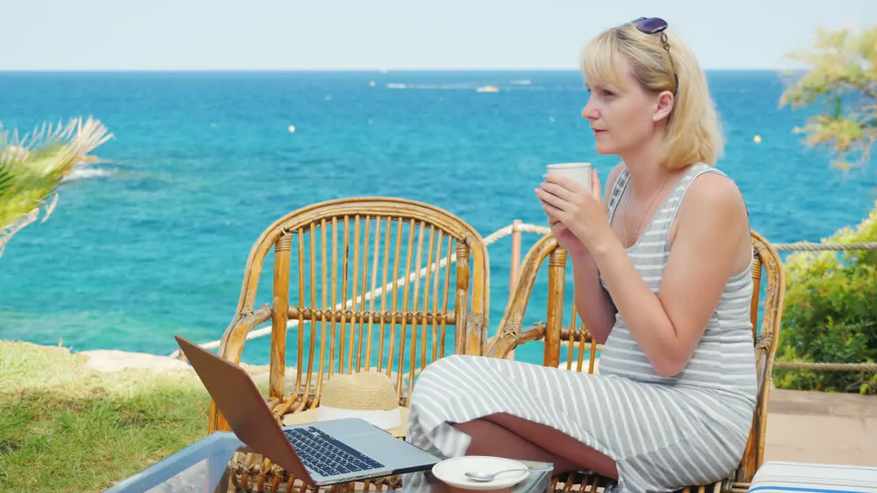 Young Woman Drinking Coffee Sitting On The Terrace Overlooking The Sea Next To The Laptop Perfect Fr