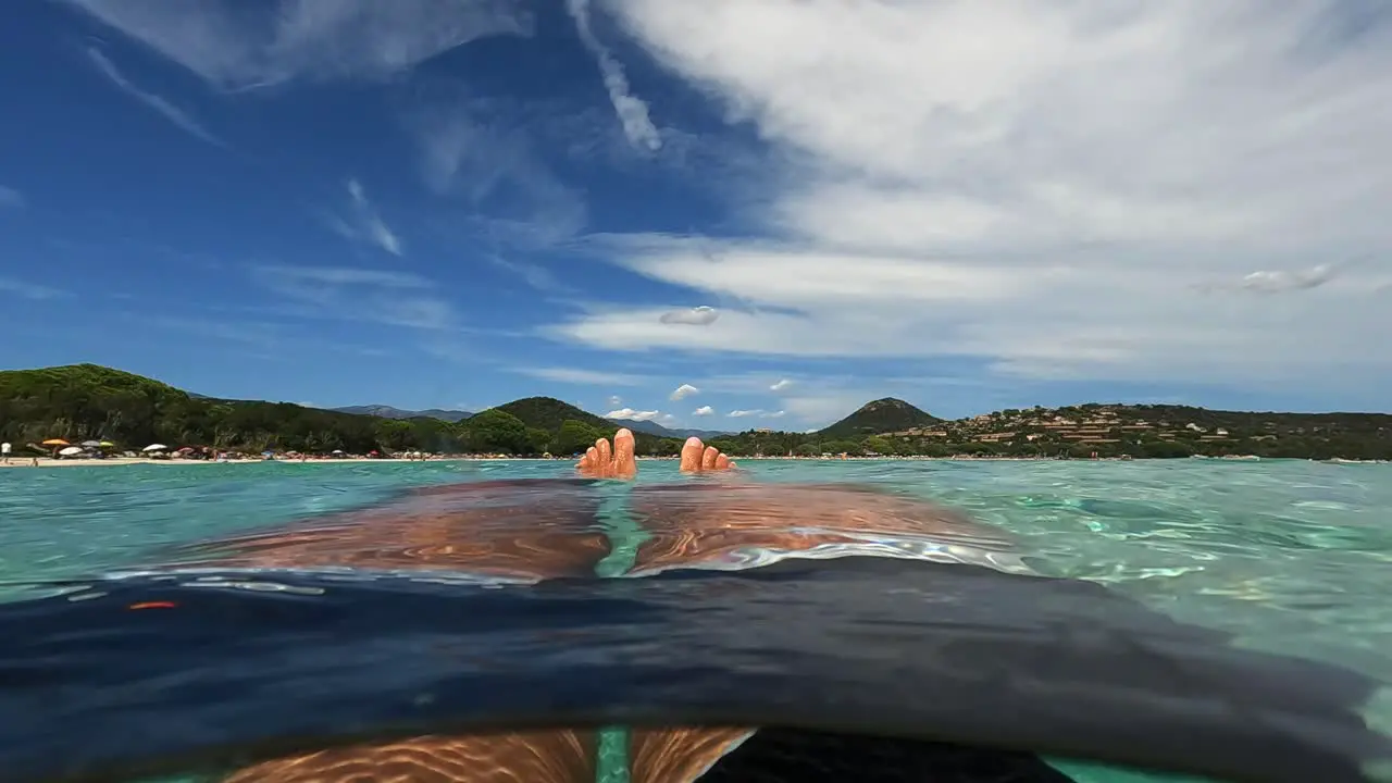 First person low angle pov of man legs and feet relaxing while floating on seawater at Santa Giulia beach in Corsica island France