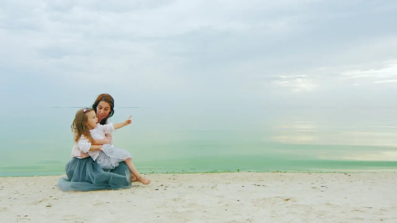 Young Mother With A Girl Three Years Sitting On The Beach Chatting