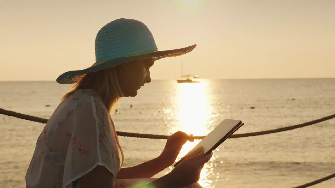 A Woman Uses A Tablet On Vacation Sits Against The Background Of The Rising Sun Above The Sea Always