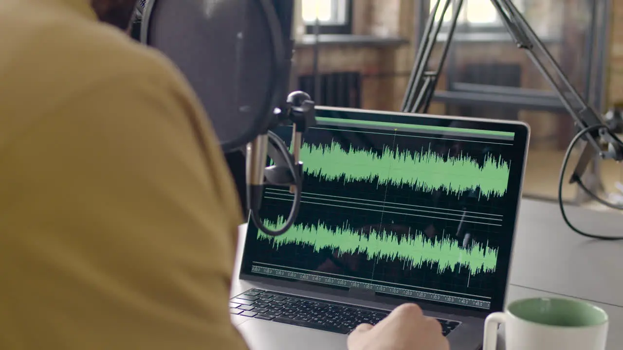 Rear View Of A Man Sitting On A Table Adjusting The Equalizer On The Laptop While Recording A Podcast