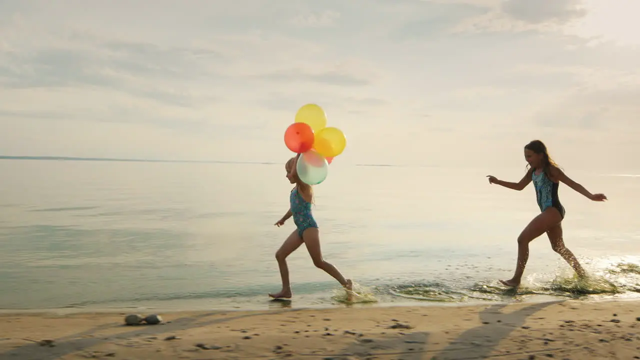 Two Girls Laughing Together Playing On The Beach Catching Up With Each Other Holding Balloons