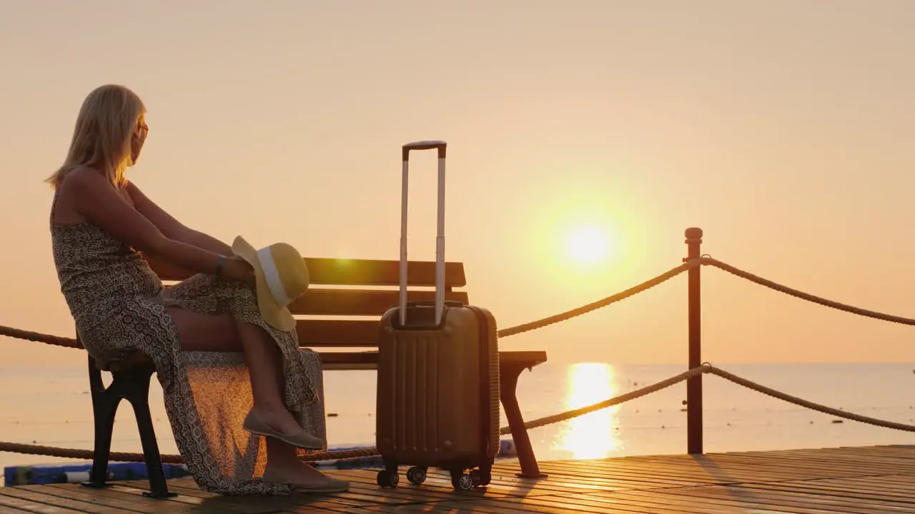 The Girl Is Waiting For Settling Into The Hotel On The Sea Pier Sits Along With Suitcases And Enjoys