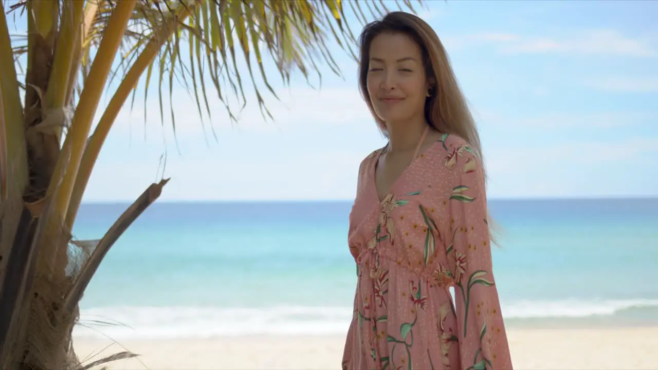 Cheerful female standing near palm on beach