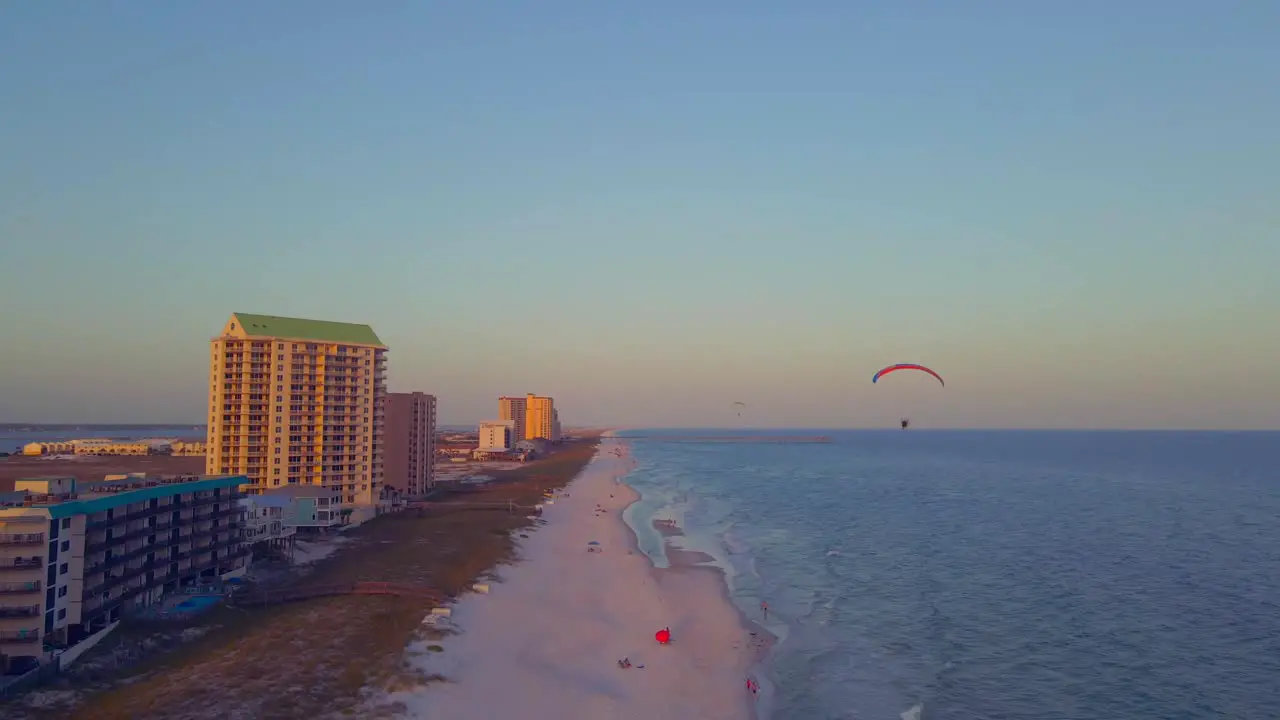 A paraglider floats through the sky over the ocean at sunset