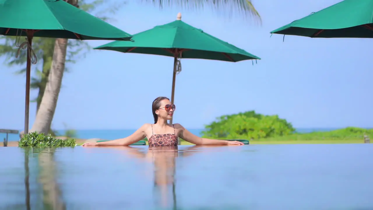 Woman Relaxing in Exotic Tropical Hotel Swimming Pool with sea and Clear Sky on background