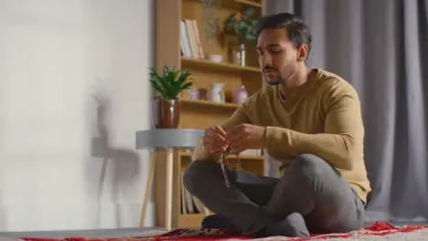 Muslim Man Praying Holding Prayer Beads Sitting On Floor At Home