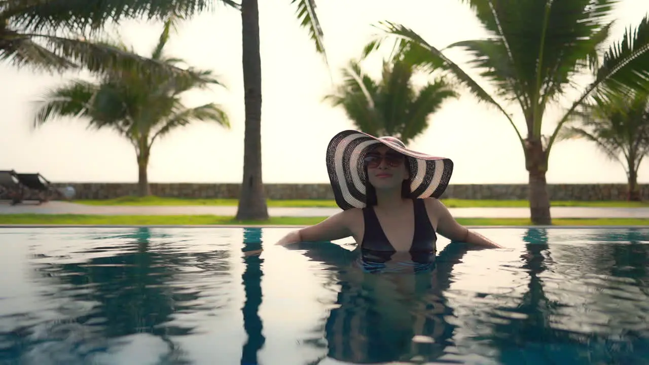 Fit luxury asian woman relaxing inside the outdoor pool on sunset