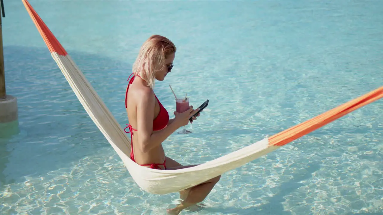 Female tourist drinking cocktail and taking selfie on hammock