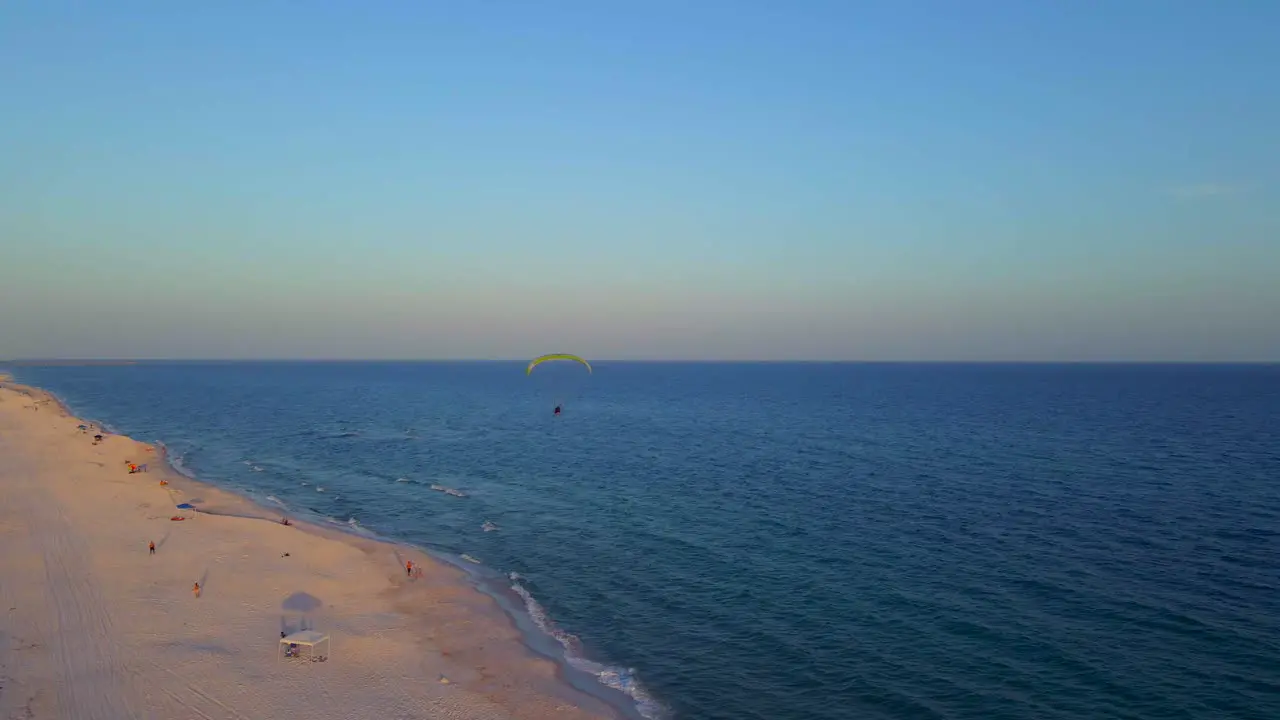 A lone paraglider flying peacefully over the ocean and beach at the end of the day