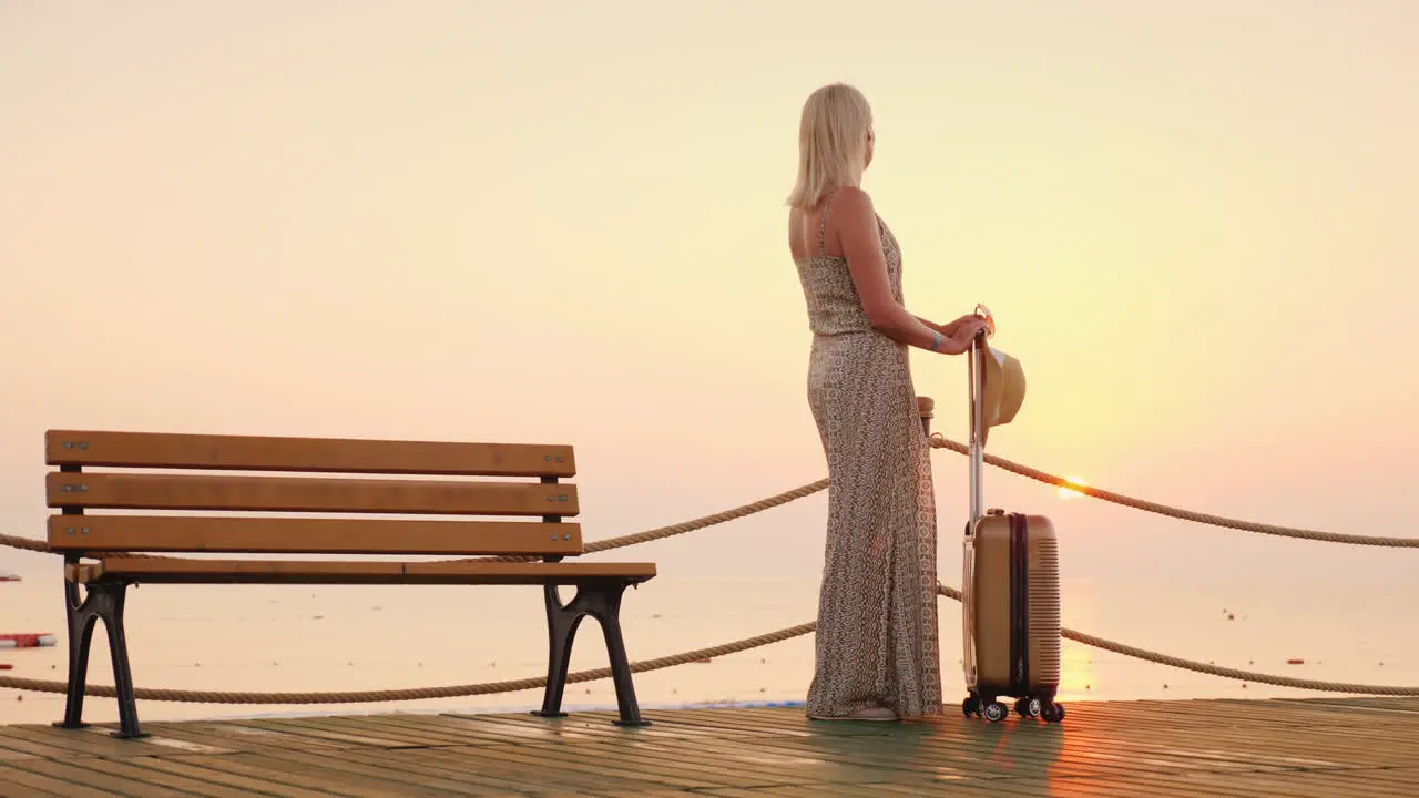 Tourist On Vacation Is On The Pier With A Suitcase On Wheels Looking Thoughtfully Into The Distance 