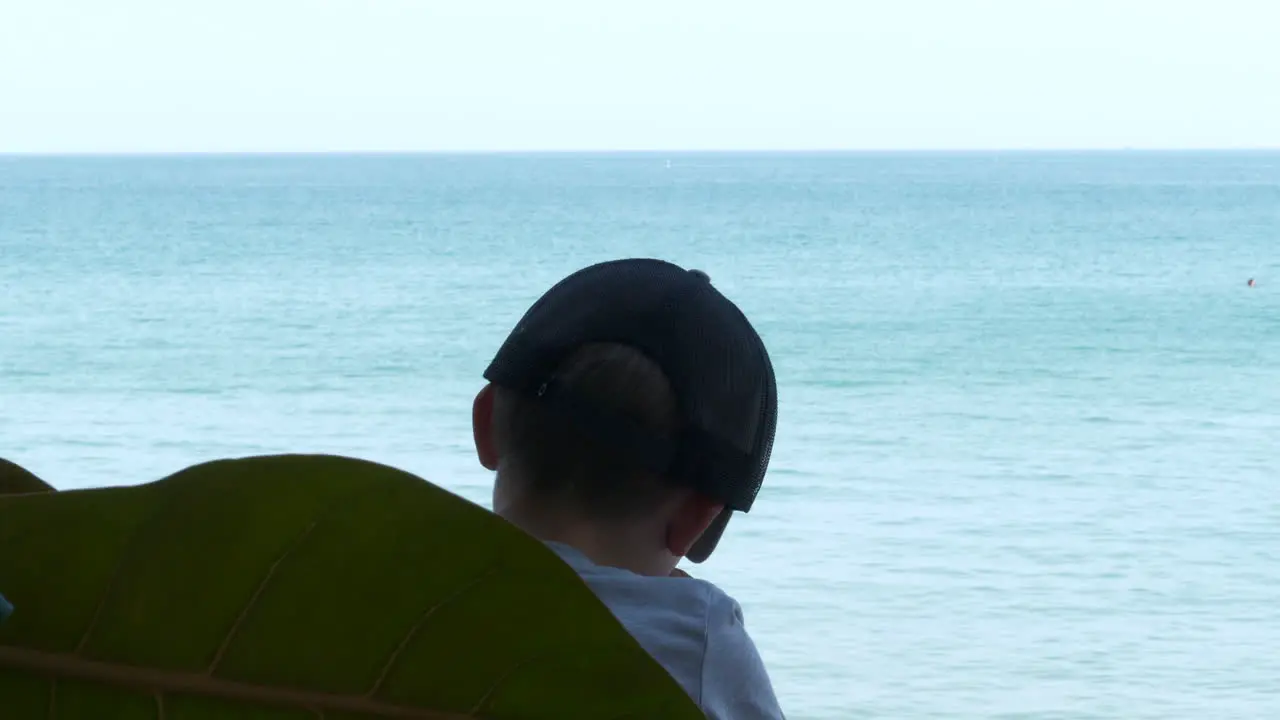 Tourist boy stuck in Thailand due to travel ban looking out Into tropical ocean ready for color grading