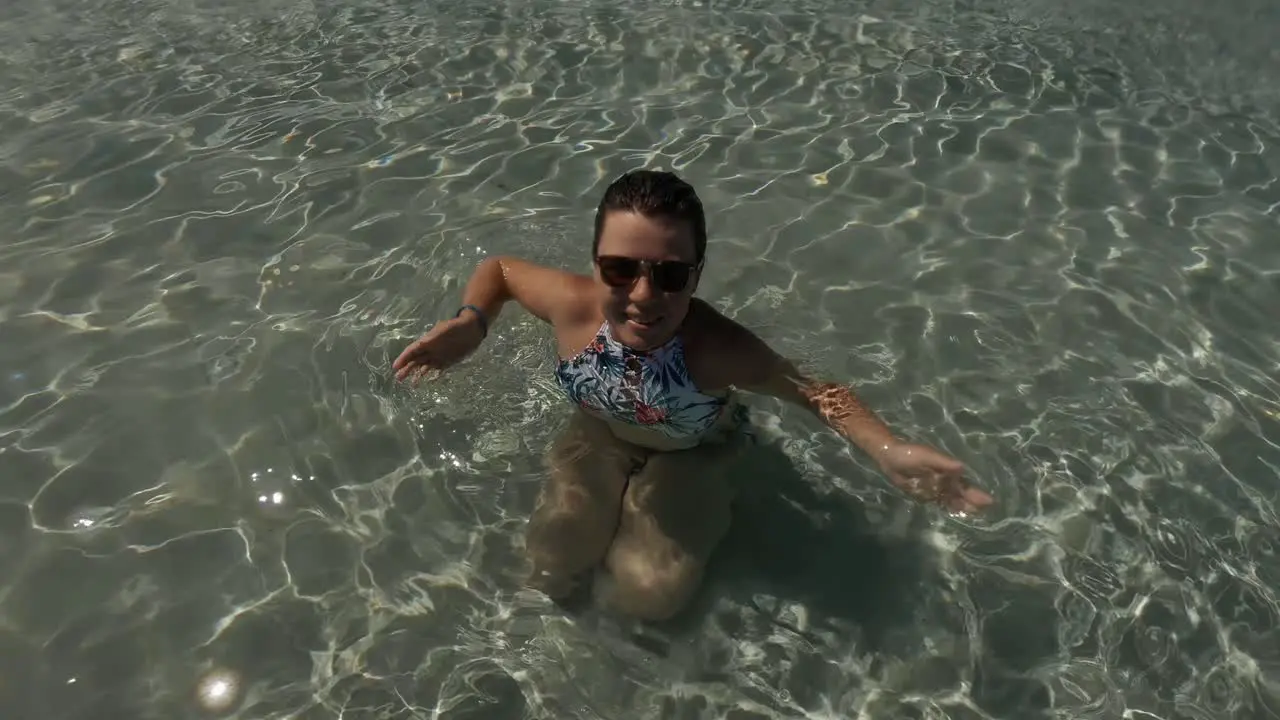 A shot of a cheerful girl wearing tropical swimming suit splashing water towards the camera