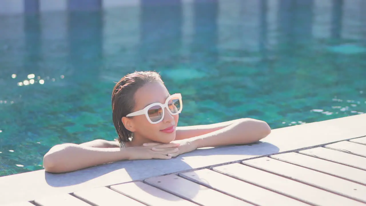 Portrait of beautiful Asian woman with white sunglasses immersed in water pool with chin on crossed hands