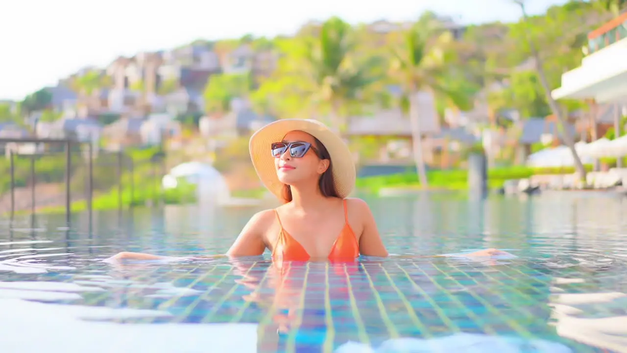 American Woman in Orange Bikini Raising Hands Up Inside Tropical Swimming Pool in Santorini Greece Happy Traveler on Vacation slow motion handheld