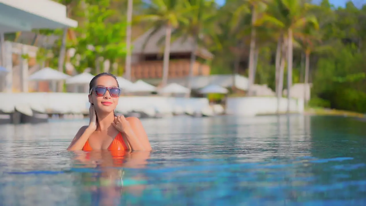 Slowmo woman inside tropical swimming pool touching her were hair and walking sensually looking at camera lense Bora Bora hotel