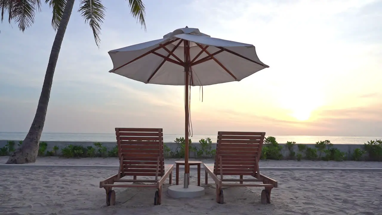 With the sun setting in the distance an empty pair of beach loungers sit under a sun umbrella on the beach