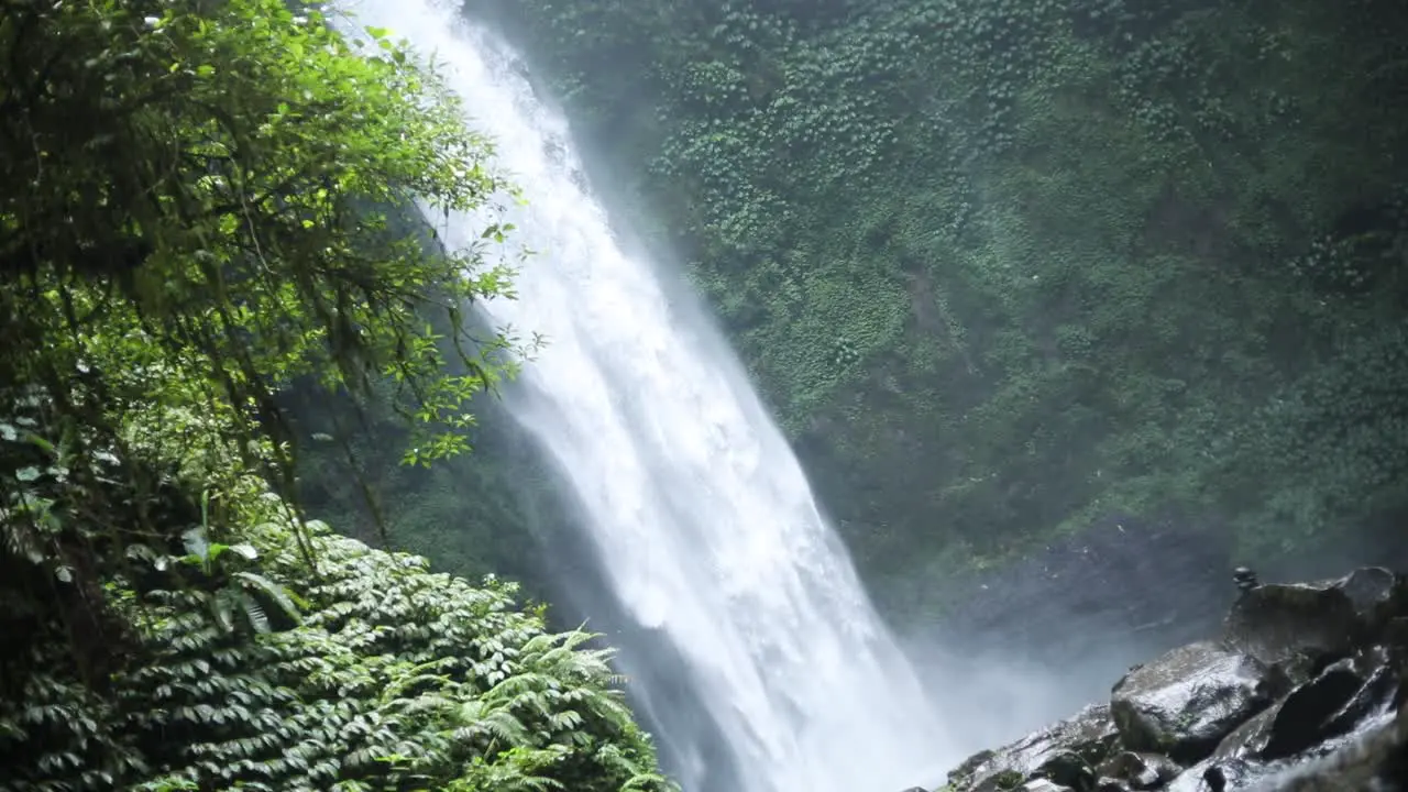 Slow motion panning shot in front of a gushing NungNung Waterfall in Bali Indonesia following a rain storm