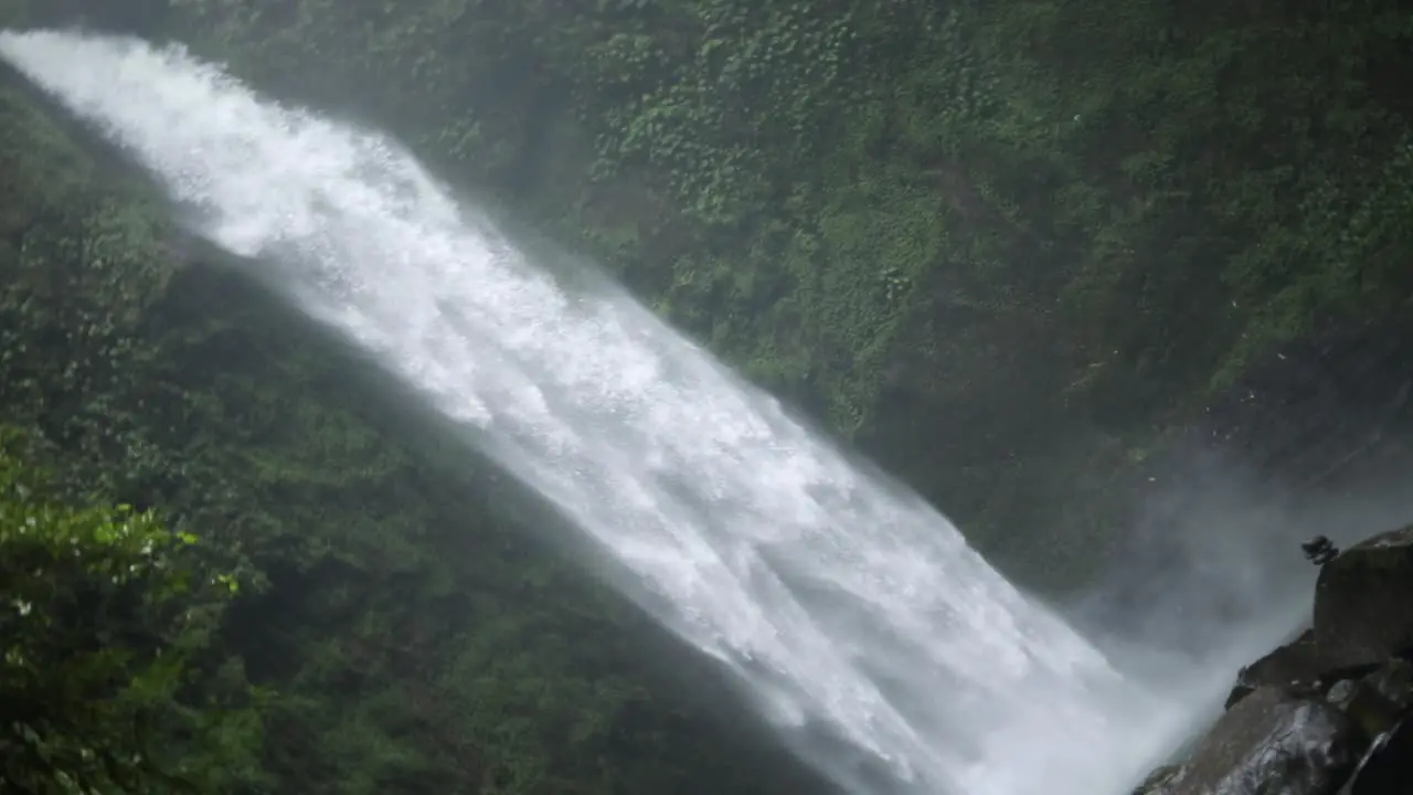 Slow motion rotating shot in front of a gushing NungNung Waterfall in Bali Indonesia following a rain storm