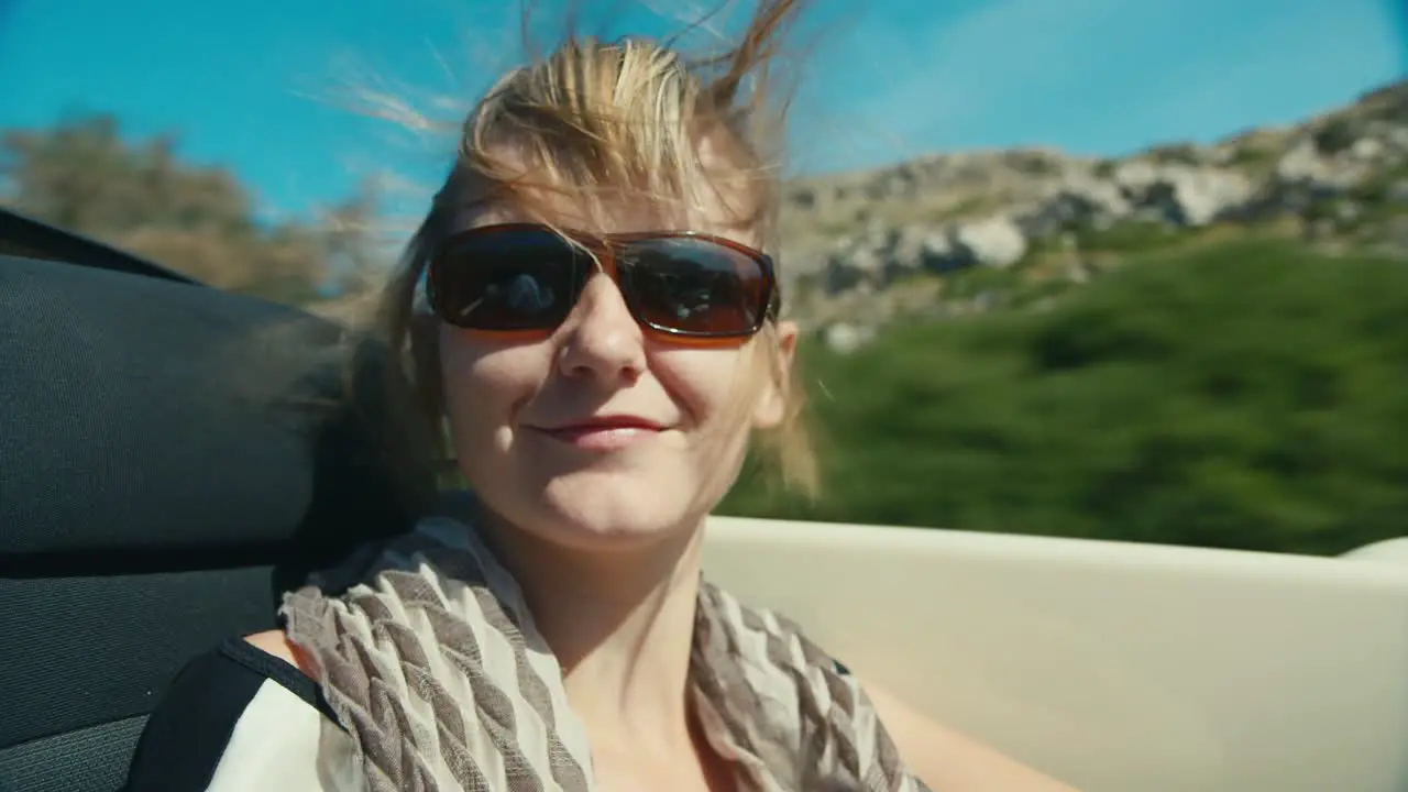 A woman in sunglasses rides in a car on a mountain road