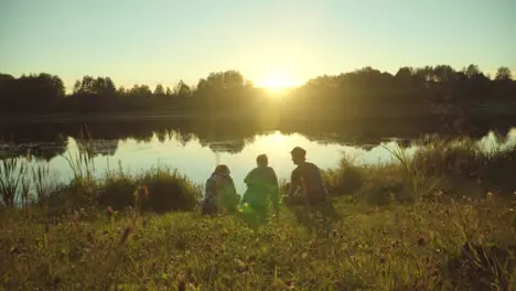 Young people enjoy vacation sitting on riverbank and meeting sunset People relax