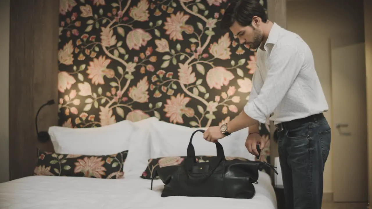 Sexy businessman putting travel bag on bed Successful man unpacking luggage