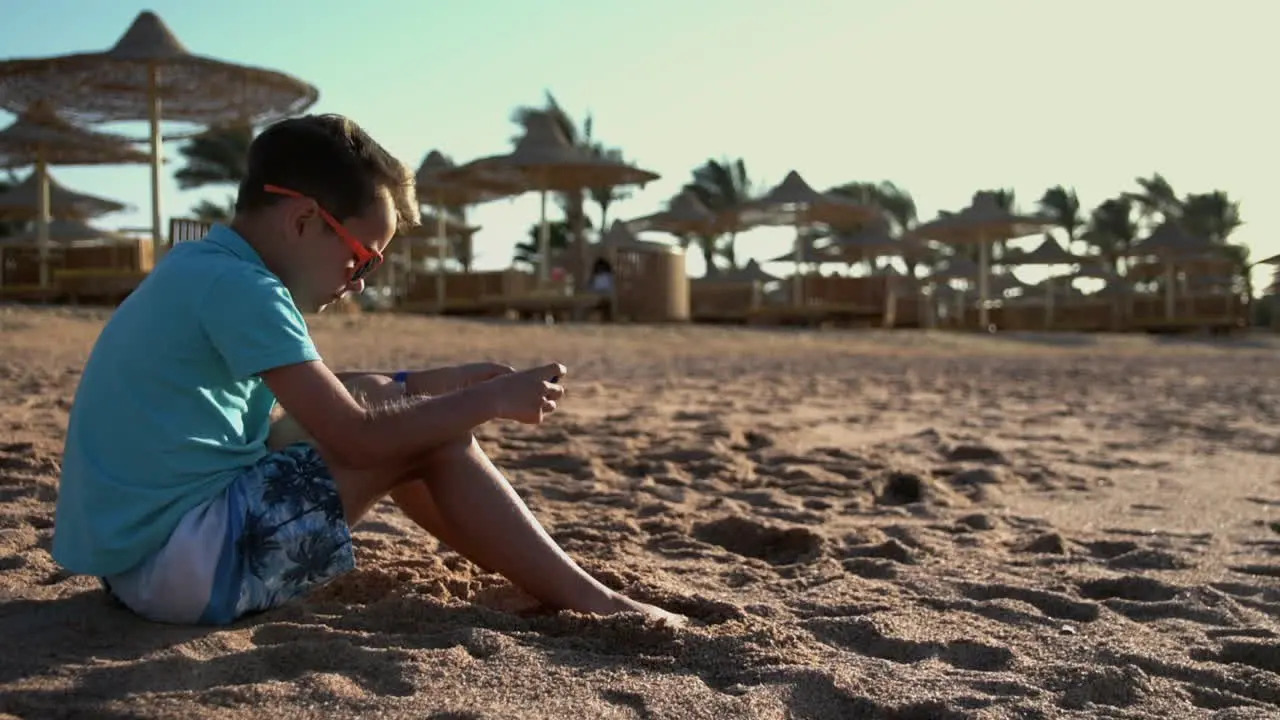 Cute teenager playing mobile phone at seashore Young man enjoying sea at beach