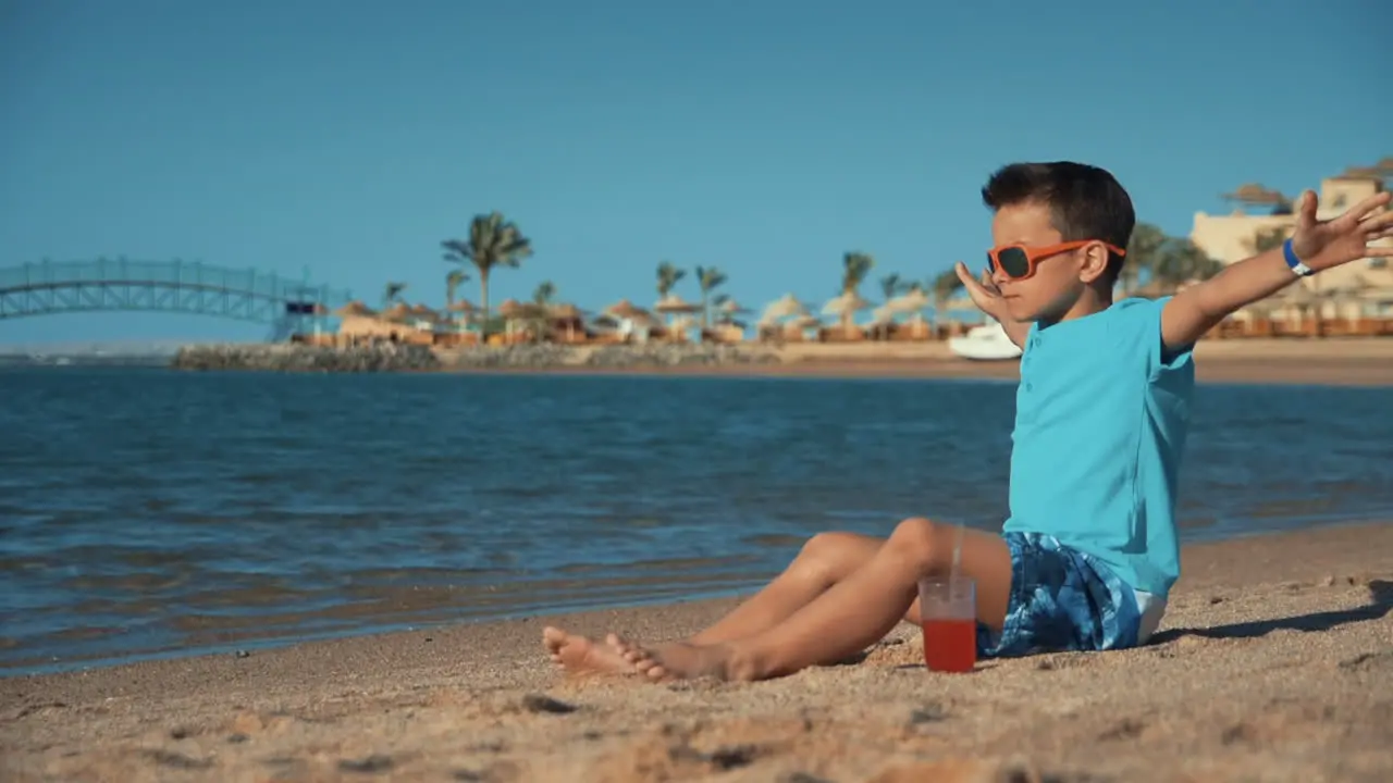 Attractive man sitting with glass of juice on sand coastline in summer vacation