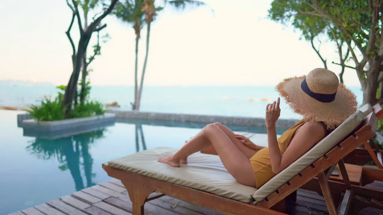 A lovely young woman looks out to sea from the comfort of her sun lounger around a resort swimming pool