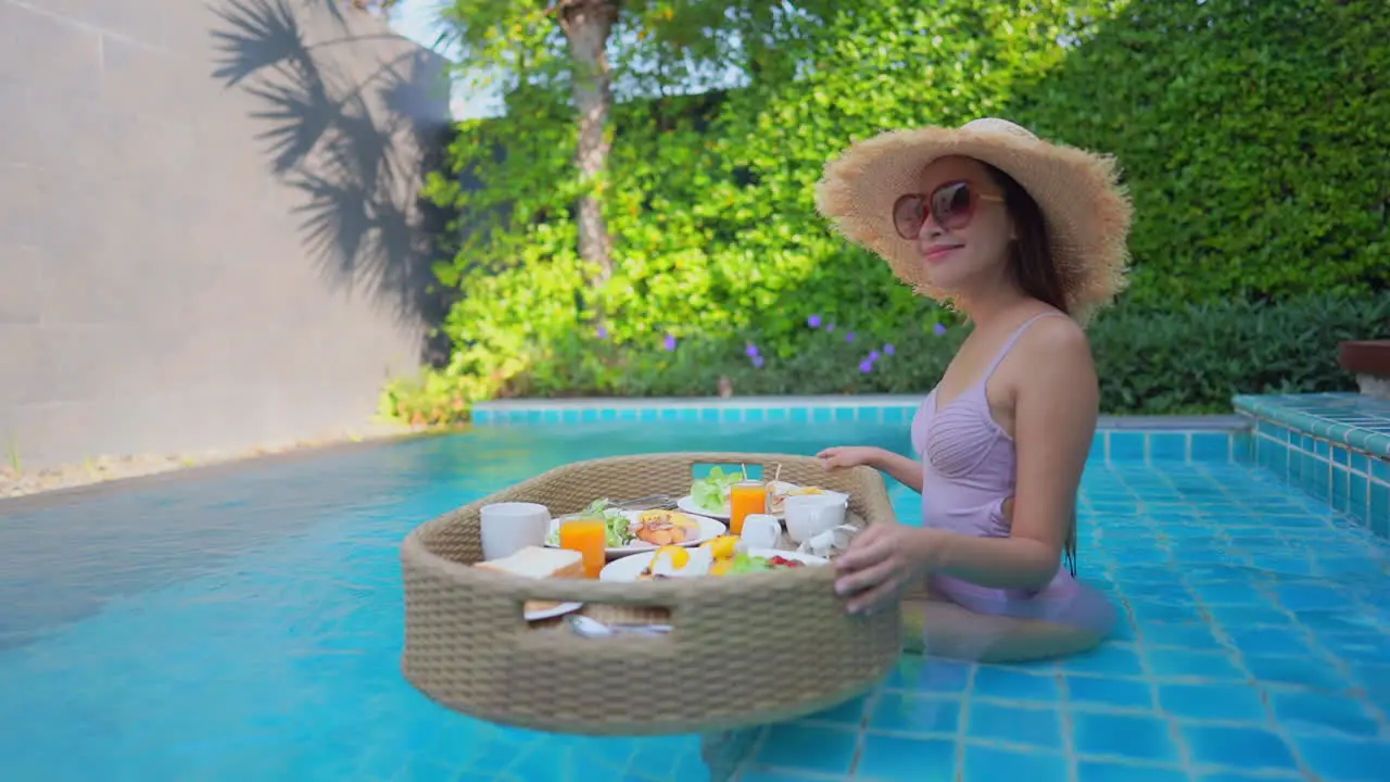 Beautiful mixed race happy Woman sitting on swimming pool holding breakfast floating tray