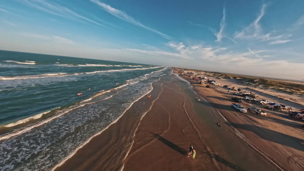 FPV Aerial drone flyover of busy Texas beach on Memorial Day Weekend full of cars and tourists playing in the ocean water and sand