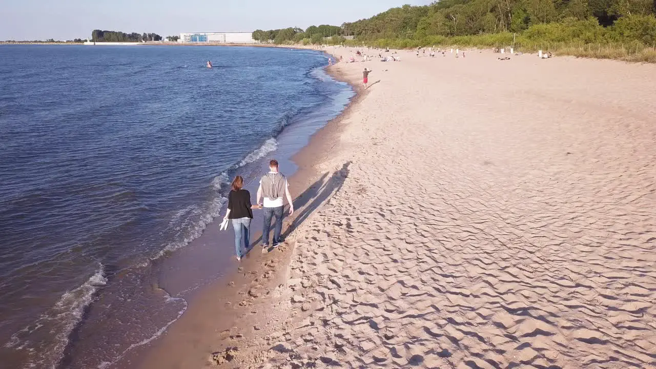 Aerial Shot Of Young Couple Walking On Beach Hugging Holding Hands