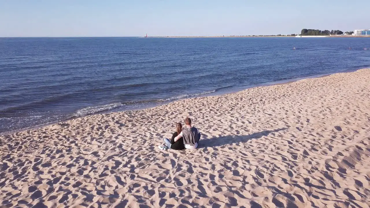 Aerial Shot Of Young Couple Sitting On Sandy Beach Hugging Holding Hands