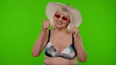 Senior pensioner woman tourist in swimsuit bra red sunglasses and hat dancing celebrating smiling