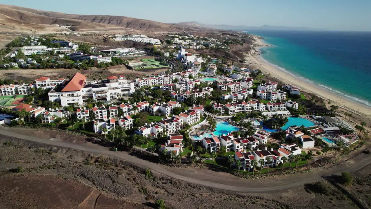 Coastal resort in Fuerteventura with white buildings pools next to a sandy beach daytime aerial view