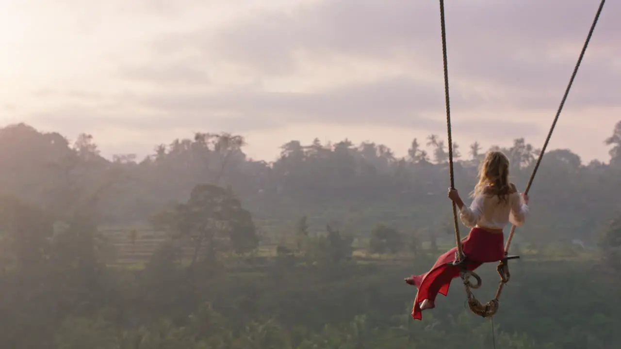 travel woman swinging over tropical rainforest at sunrise female tourist sitting on swing with scenic view enjoying freedom on vacation having fun holiday lifestyle slow motion