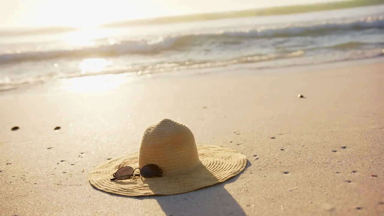 A straw hat and sunglasses rest on a sandy beach bathed in sunlight with copy space