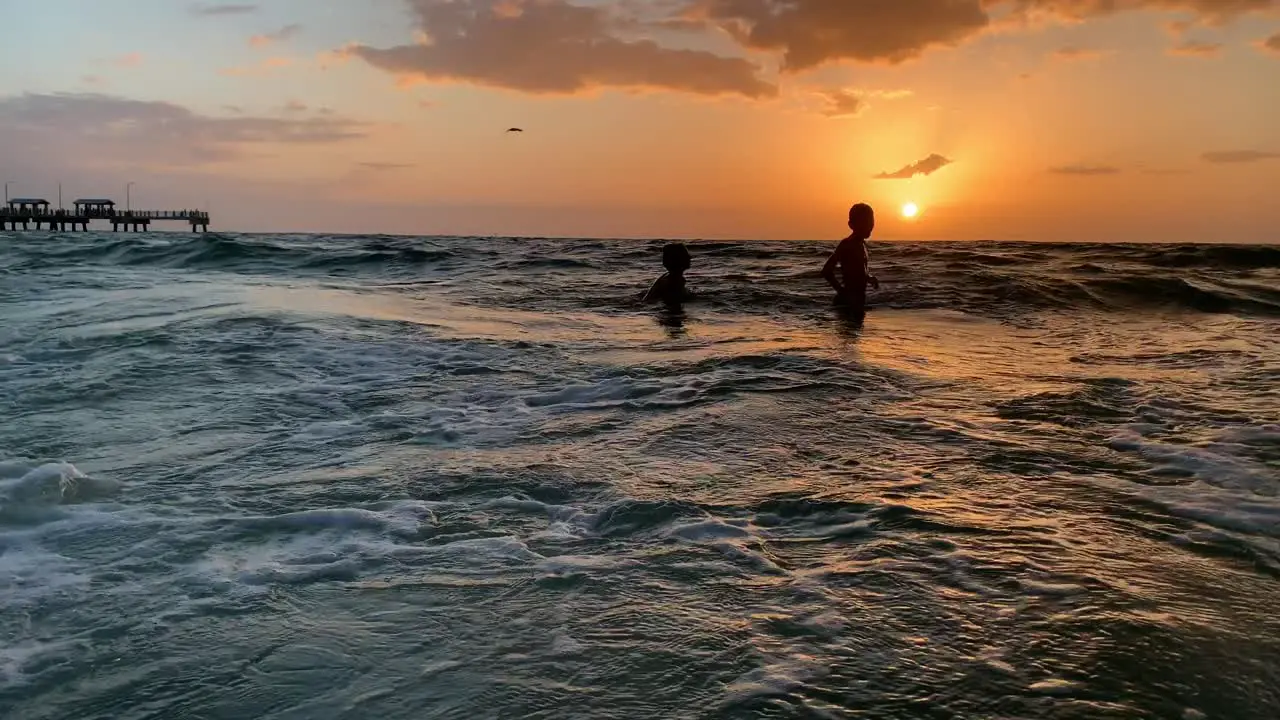 Two kids swimming jumping waves in the ocean on the beach during sunset in Florida