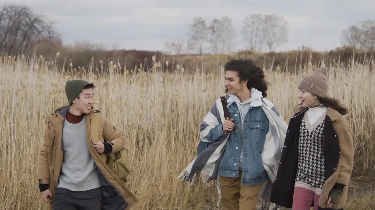 Two Teenage Boy And Girl And Teenager Boy With Long Hair Wearing Winter Clothes Walking In A Wheat Field On A Cloudy Day