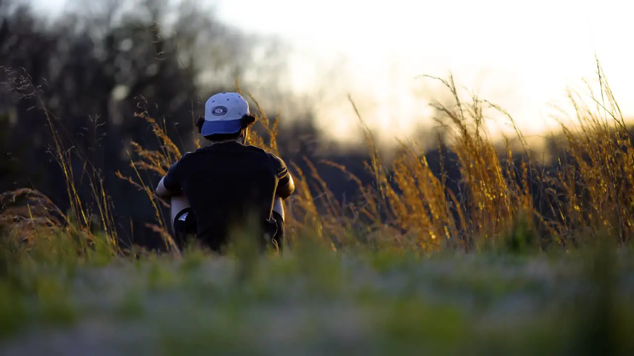 Boy Sitting In Grass During Sunset