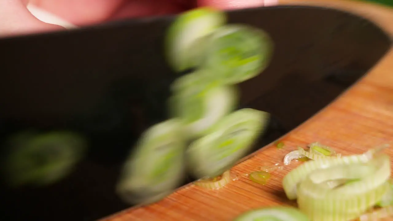 Macro cutting spring onions with a black knife on a wooden chopping board