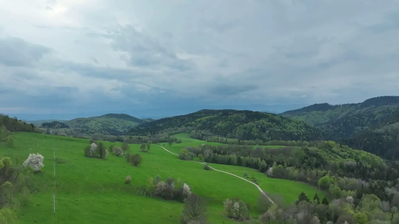 Discover the beauty of spring A drone glides low over blossoming orchards meadows and an abandoned barn all under dramatic clouds while an unpaved road winds through the landscape