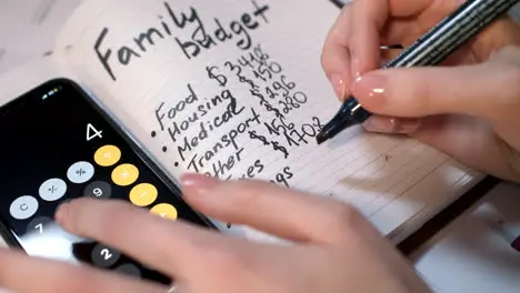 Woman calculate family budget on calculator and writing in notebook