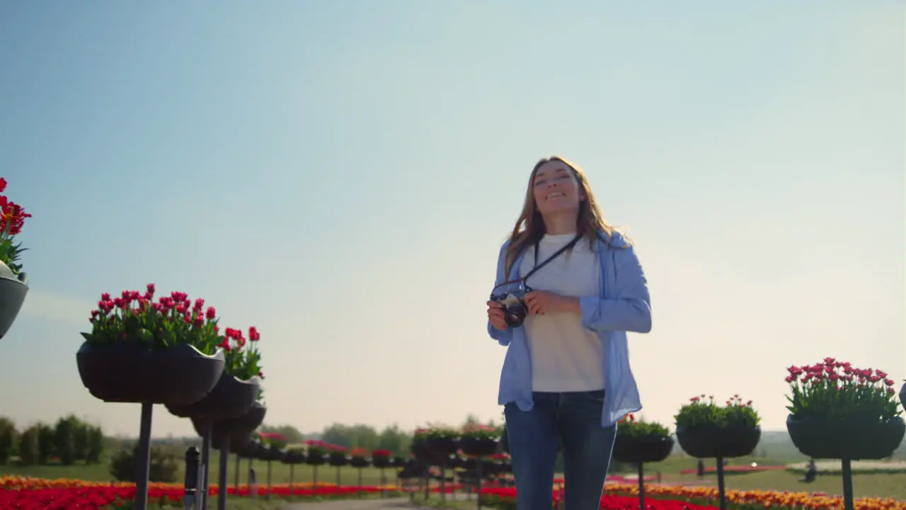 Happy female photographer running in slow motion in blooming park in sunny day