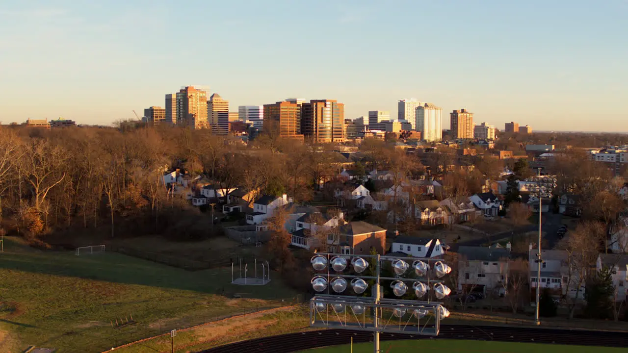 Slow descent from a downtown city skyline to a football field stadium light in foreground