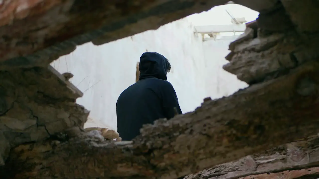 Young man teenager sitting high on a beam in an abandoned house puts on his hood