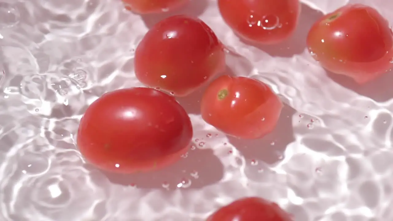 Small tomatoes falling into a container with water for cleaning