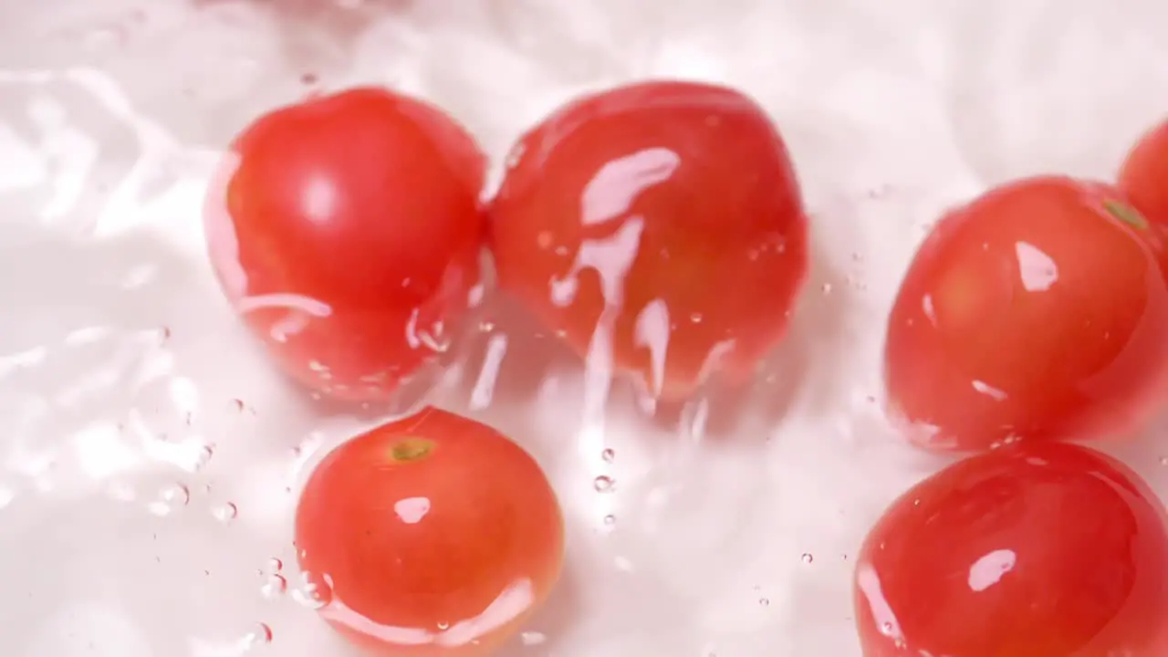 Slow motion of small tomatoes falling into a container with water for cleaning