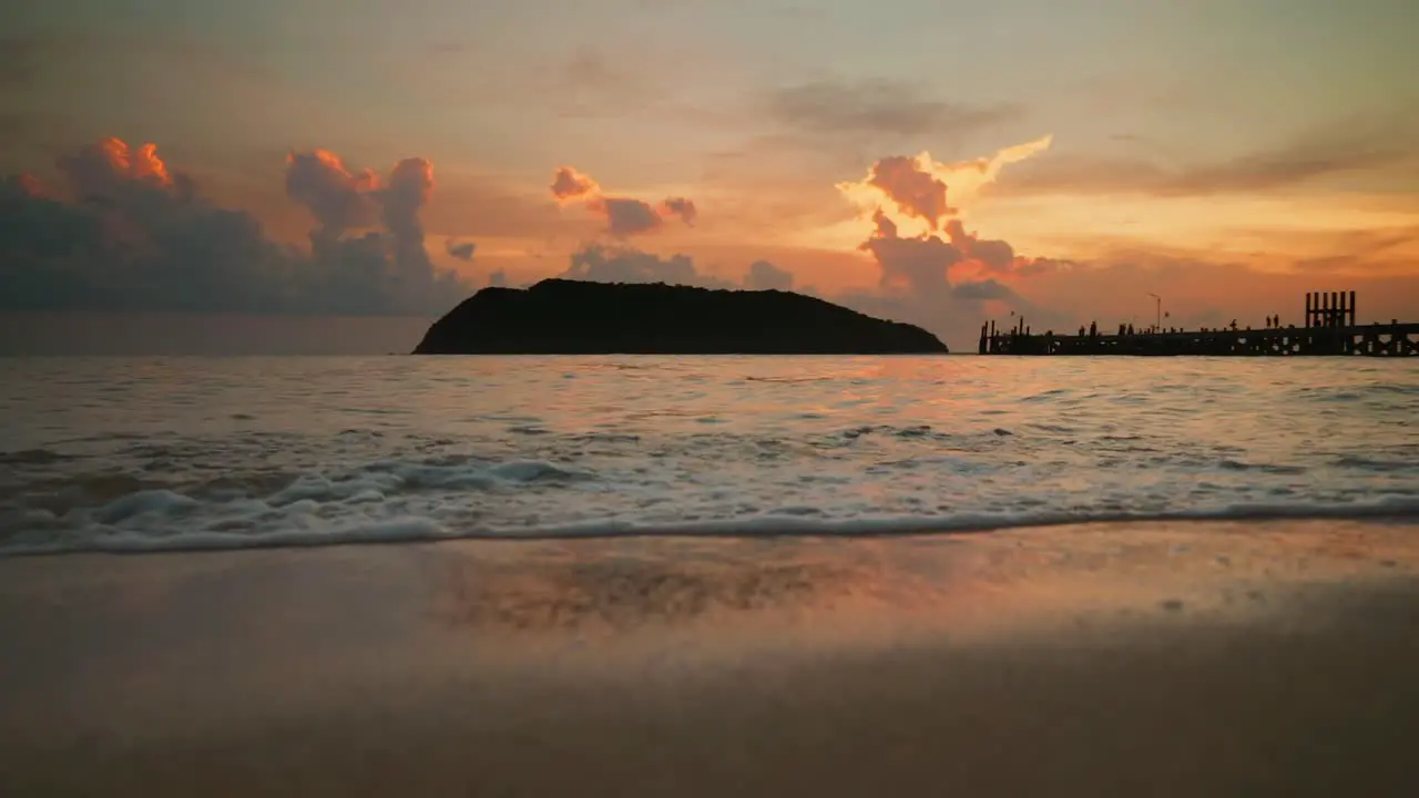 Ocean waves on the beach against island and pier during sunset in Slow Motion