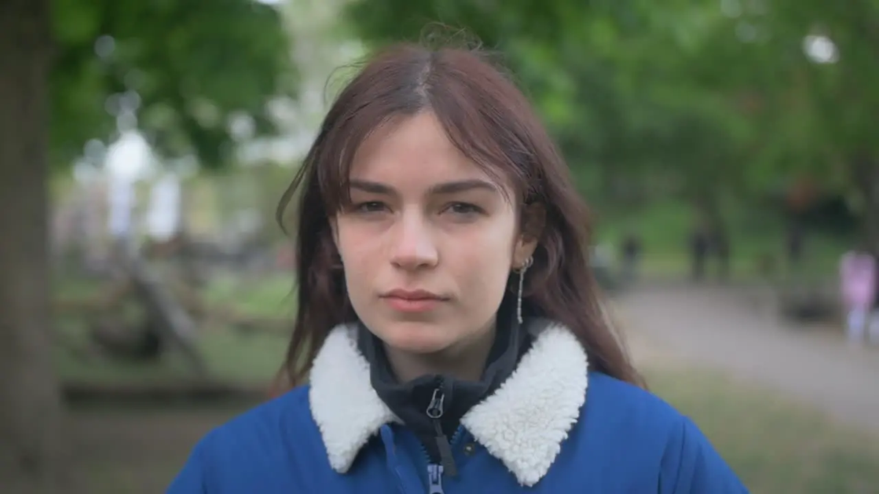 Brunette woman in denim jacket looking seriously at the camera in a park in slow motion